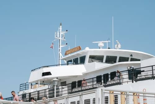 White ferry boat with black railings against a blue sky with Nantucket on its masthead.
