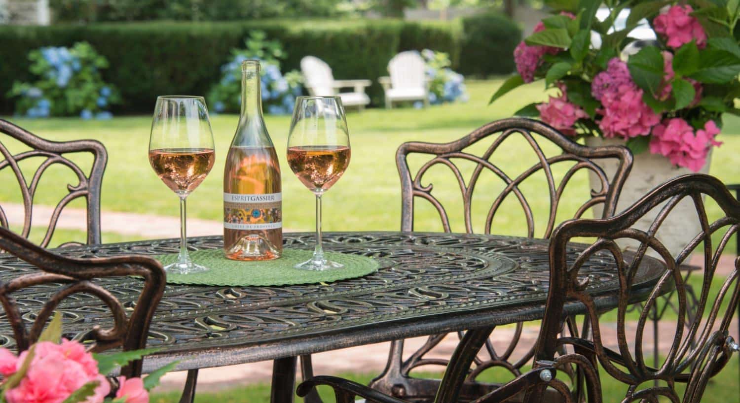 Rod iron patio table and chairs with wine bottle and two wine glasses full of wine on top