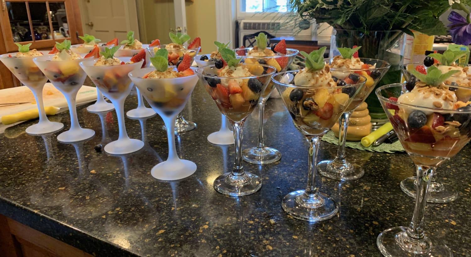 Clear and frosted martini glasses filled with fruit and yogurt topped with a few mint leaves