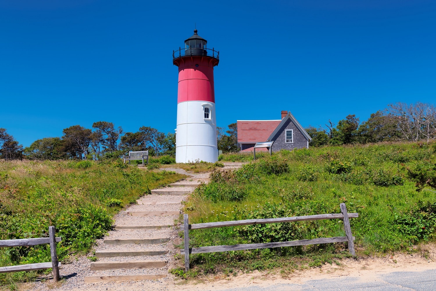 steps leading to a red, white and black lighthouse against a blue sky