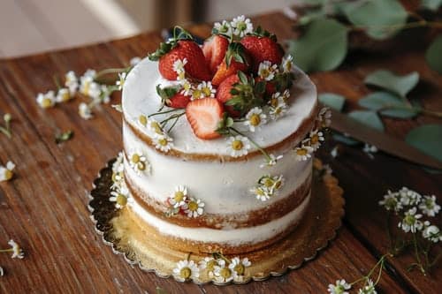 Small white frosted wedding cake with strawberries and daisies