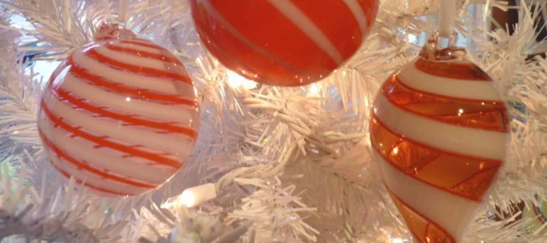 Close of of 3 red and white ornaments on a lighted white Christmas tree.