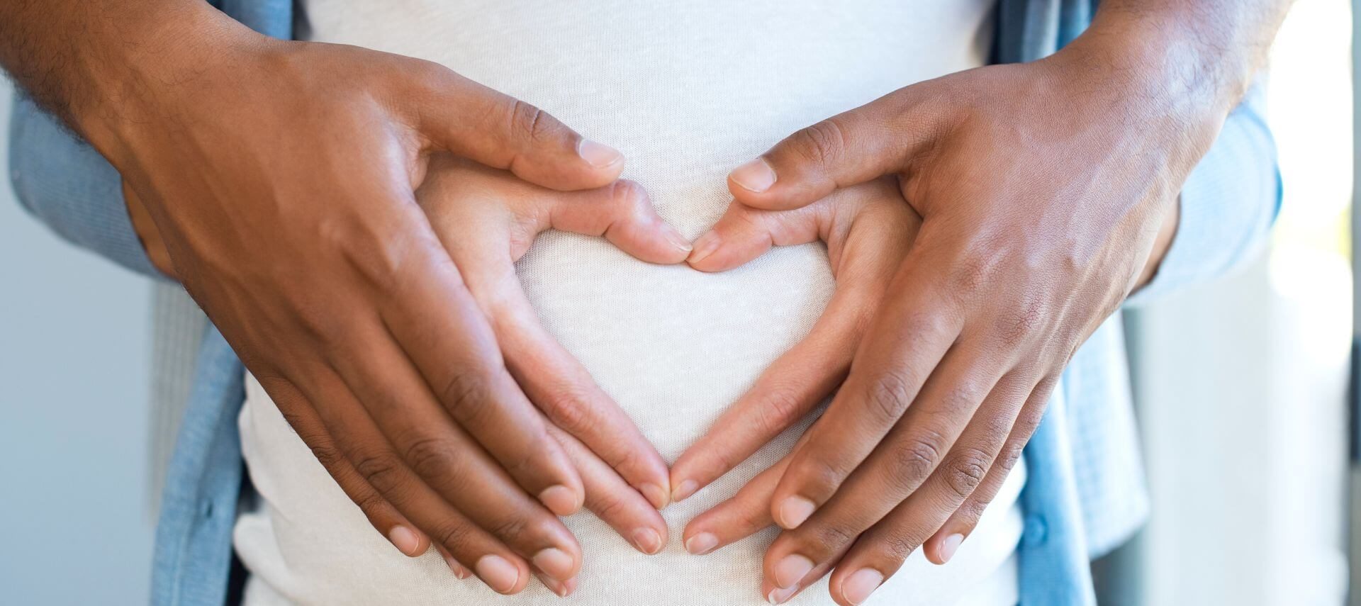 Man and woman’s hands on pregnant tummy shaped like a heart