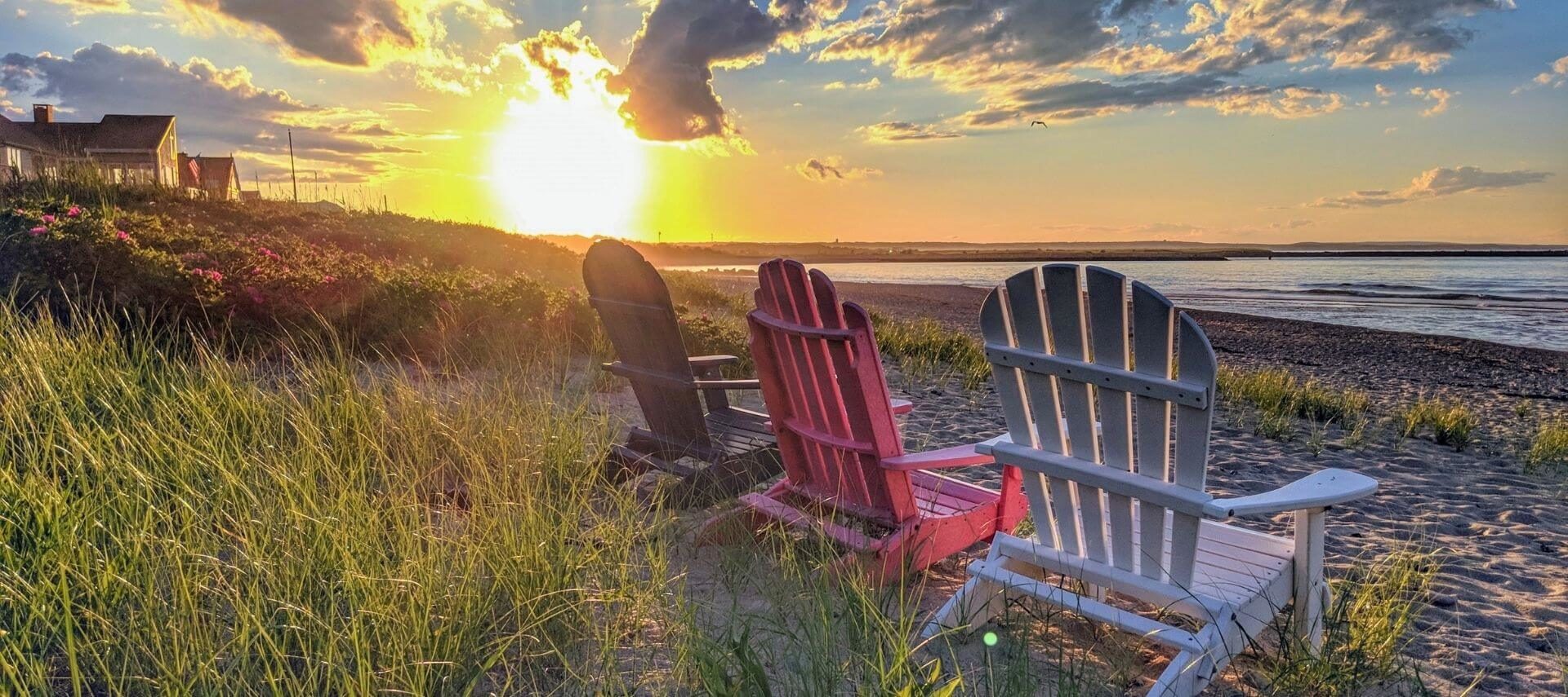 Three Adirondack chairs on a Cape Cod beach at sunset.