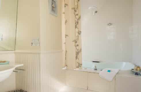 Bathroom with cream walls and tiled floor, white sink, and shower and tub combination all tiled in white with cream and floral shower curtain