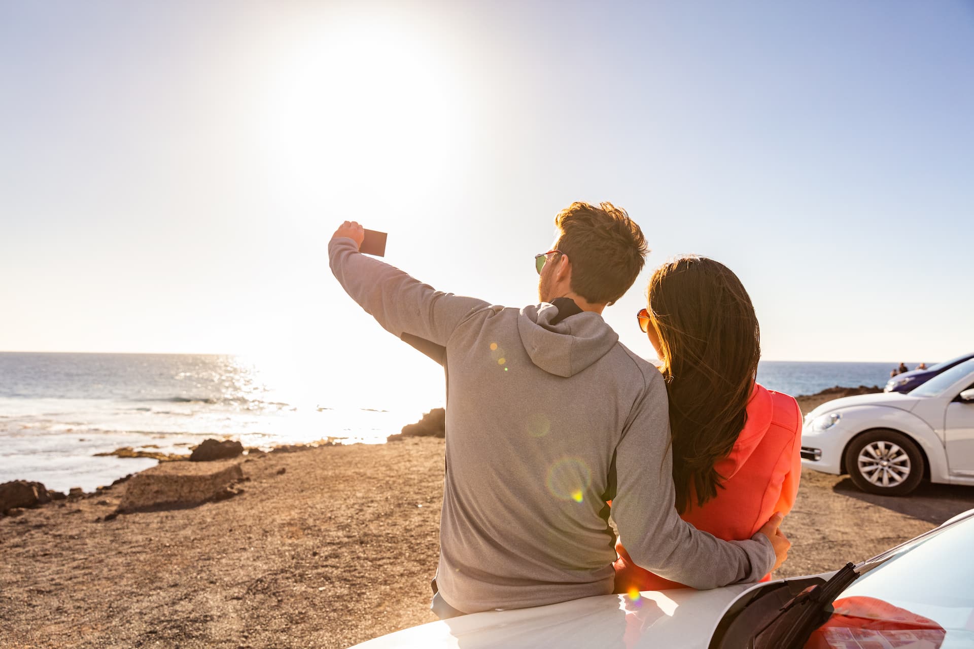 Couple taking a photo of the ocean while leaning on a car