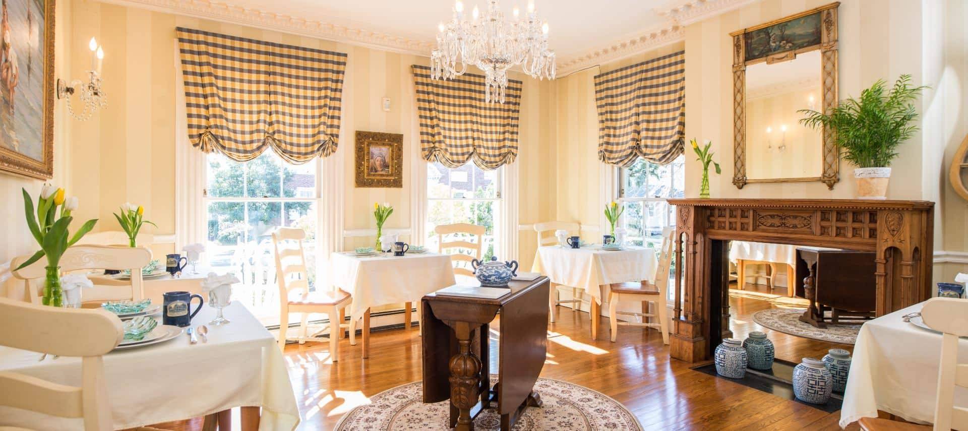 Dining area with wooden tables and chairs with white tablecloths, hardwood floors, crystal chandelier, and wooden ornate fireplace mantel